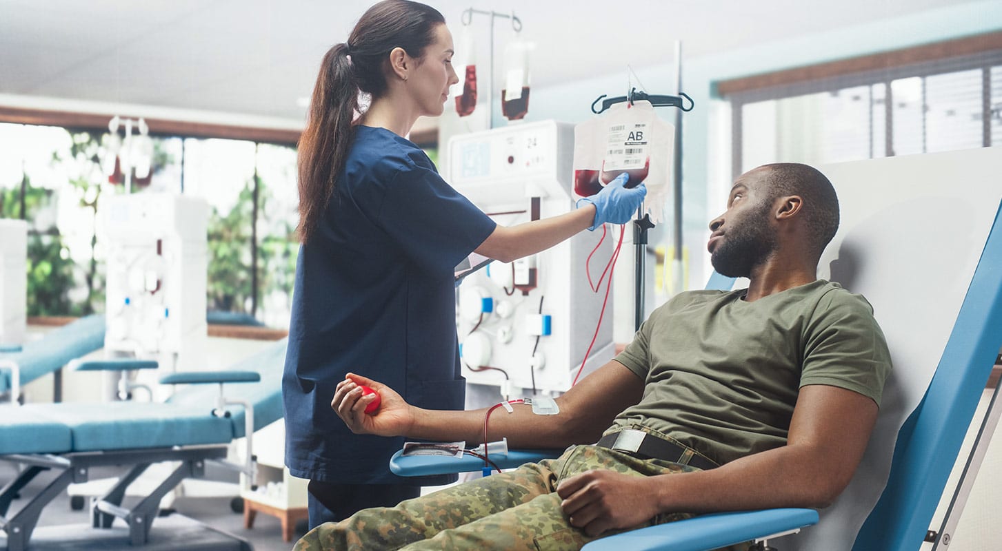 Medical professional taking blood from a male patient in military uniform in a hospital.